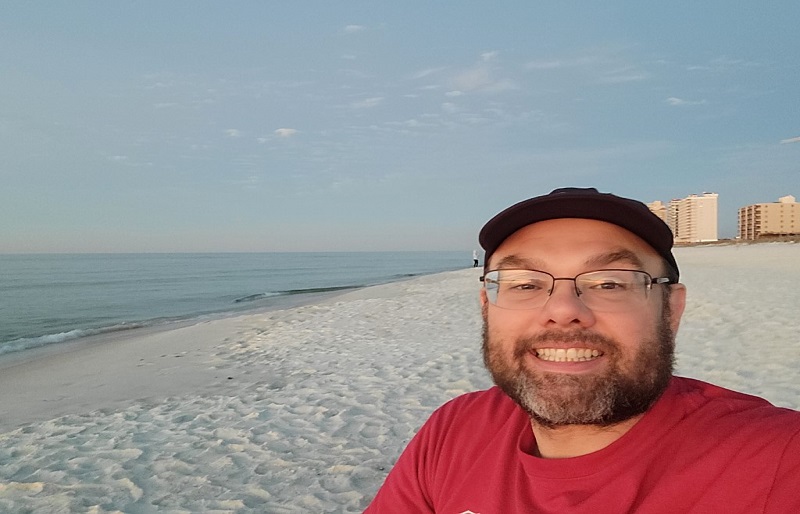 Smiling photo of the owner, looking at the camera, sitting on Perdido beach